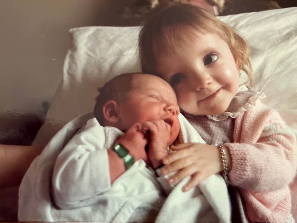 2 year old Stella lovingly cradles her new baby sister who is wearing a hospital tag on her wrist.
