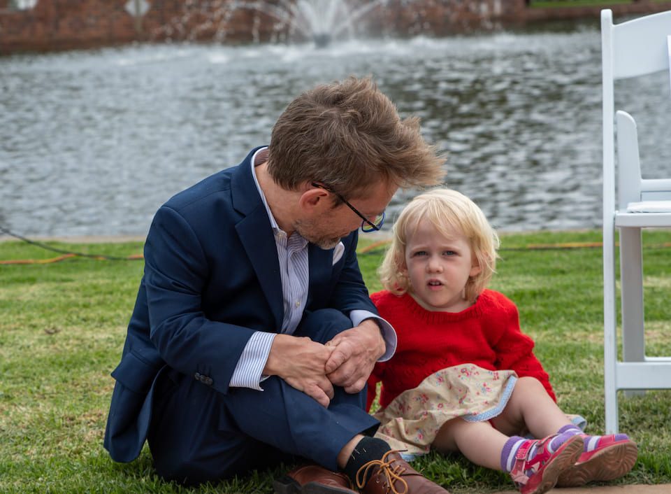 A young child sitting on the grass talking with a gentleman in a suit
