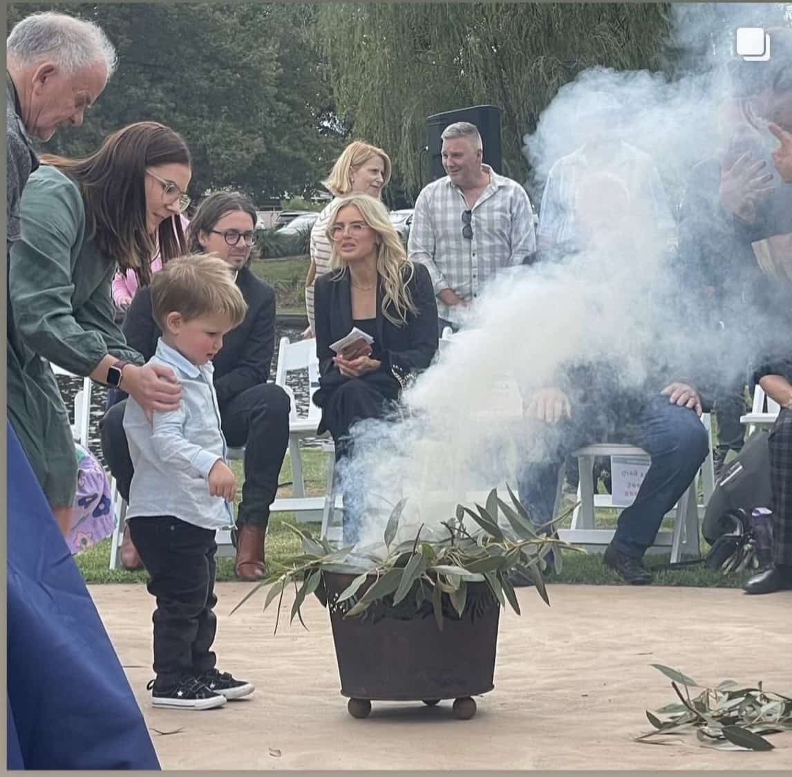 A young boy wearing a blue shirt adding leaves to the fire at the smoking ceremony